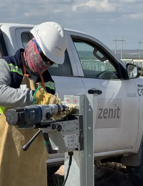 trabajador atornillando poste con atornillador electrico y elementos de seguridad delante de camioneta con logo de Zenit